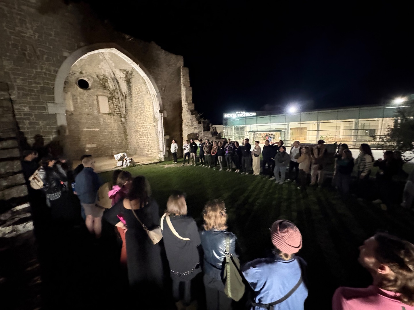 Creative Pro team standing in a circle at night beside a lit stone arch ruin in Slovenia